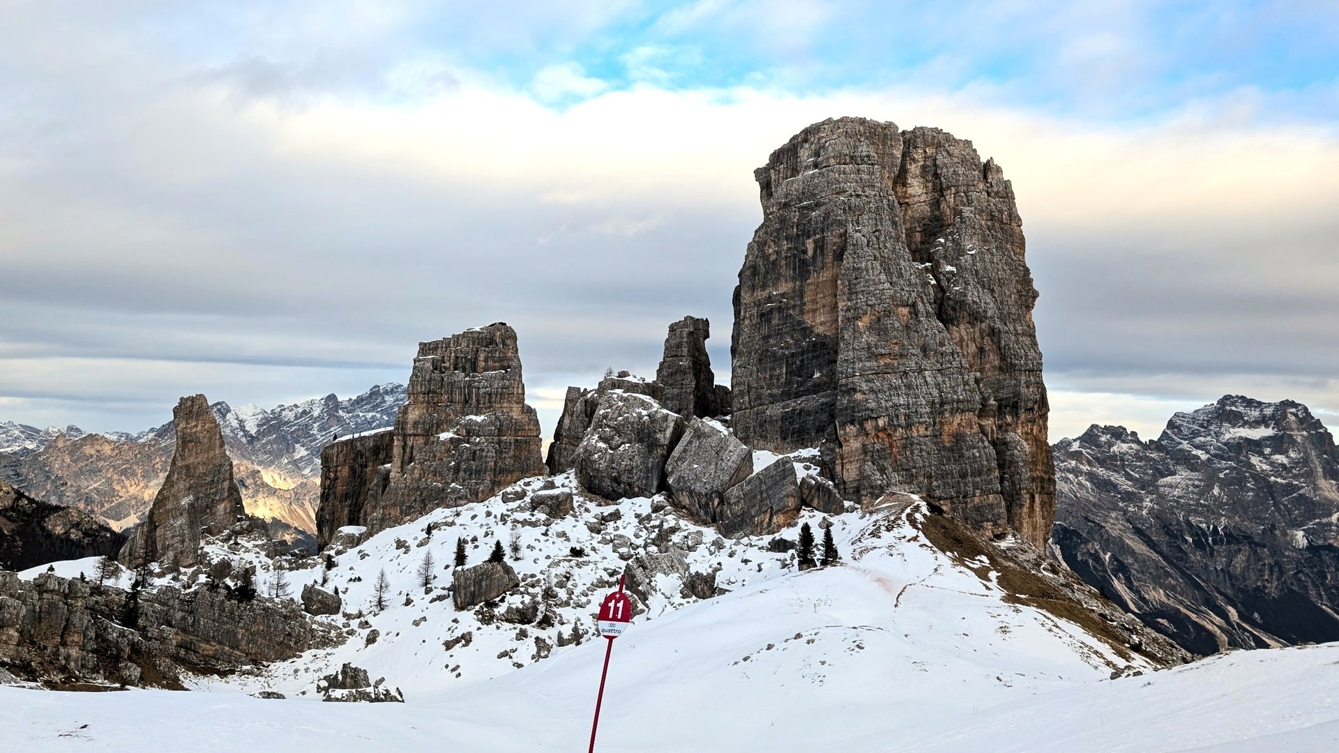 The Cinque Torri rock towers above a snowy piste, with a red piste marker in the foreground.