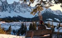 Person sitting at a viewpoint overlooking the Lago di Carezza and surrounding snowy peaks.