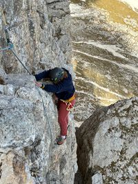Climber pulling through the upper Via del Gracchio moves with Val di Fassa meadows below.