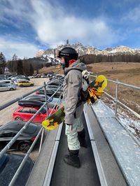 Snowboarder riding magic carpet lift from Socrepes parking area with Tofana mountain range in background, Cortina d'Ampezzo
