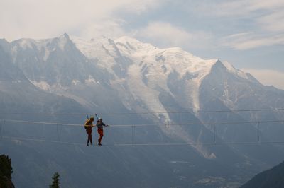 Daysi and David crossing a via ferrata cable bridge above snowy peaks