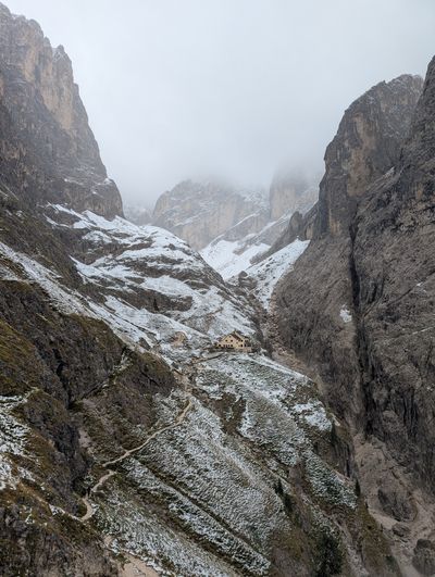 Rifugio Bergamo emerging from the mist in a snow-covered valley.
